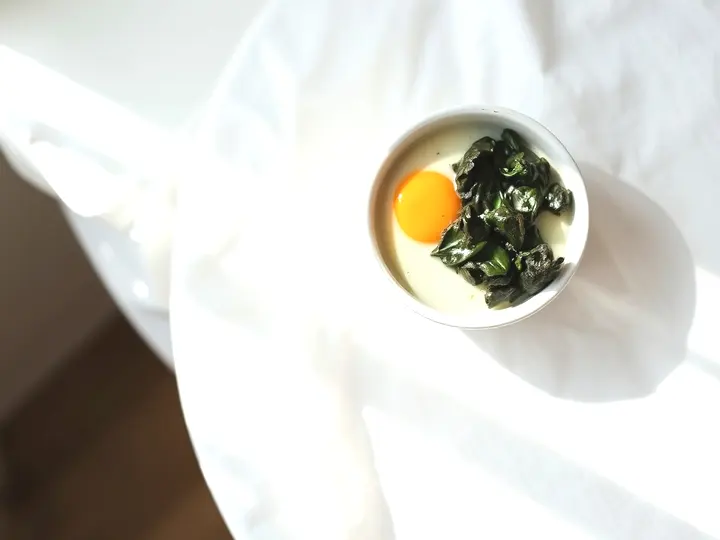 Huevos al plato con nata y espinacas en una cazuelita, vistos desde arriba